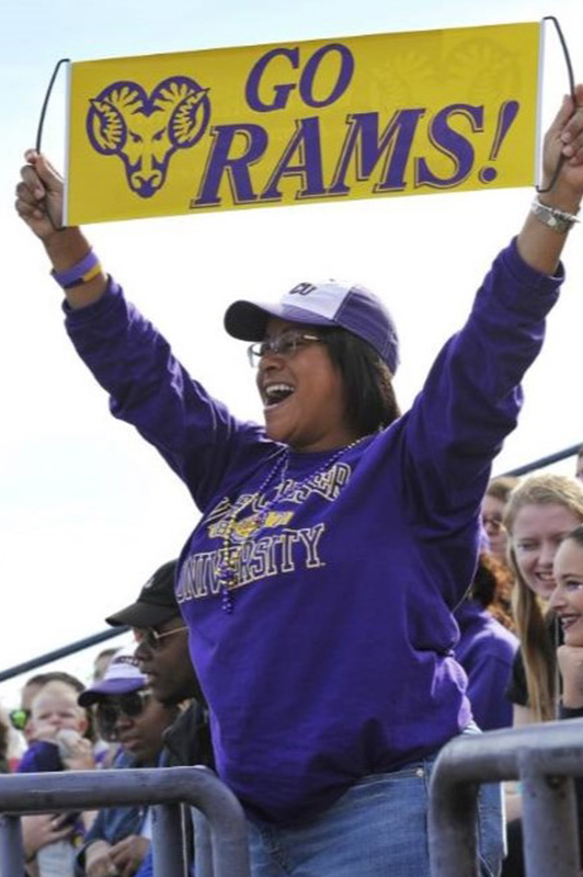 Homecoming event photo - student at a homecoming event with West Chester University sweatshirt and WCU hat holding up a sign with the Ram logo and the words Go Rams!