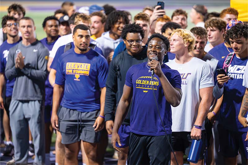 A group of students gathered while at Ram Rally Under the Lights, most of them are wearing WCU tshirts and the WCU Student in front is saying something through a microphone