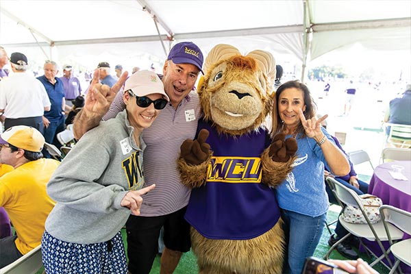 Three people in WCU gear smile and pose with Rammy while holding up the WCU ram hand symbols