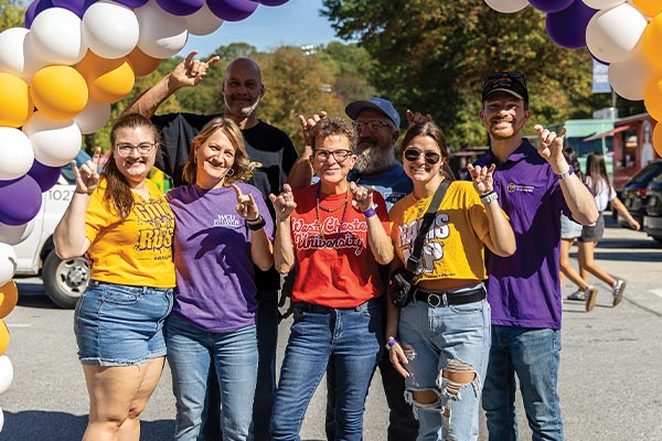 A group of people in WCU gear are smiling and posing with their Ram hand symbols up