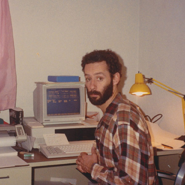 1983 - Chris Fiorentino sitting at a desk in front of a computer looking at the camera.