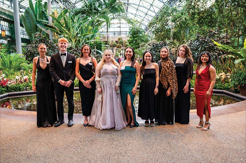A group of people wearing fancy gowns and suits pose for a group photo