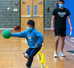 Child running drills with a green basketball. Adult watching in the background.