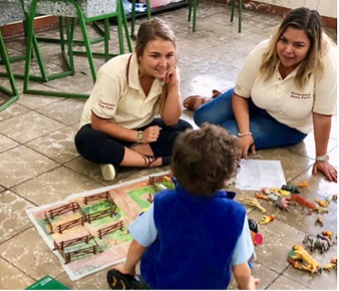 Two college students sitting on the floor with a child in a classroom setting.