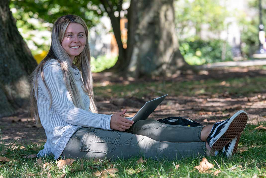 

						Student sitting in the grass on a laptop

					